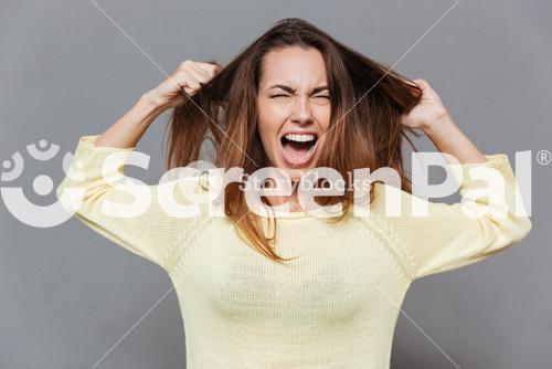Portrait Of A Frustrated Angry Woman Screaming Out Loud And Pulling Her Hair Out Isolated On The Gray Background